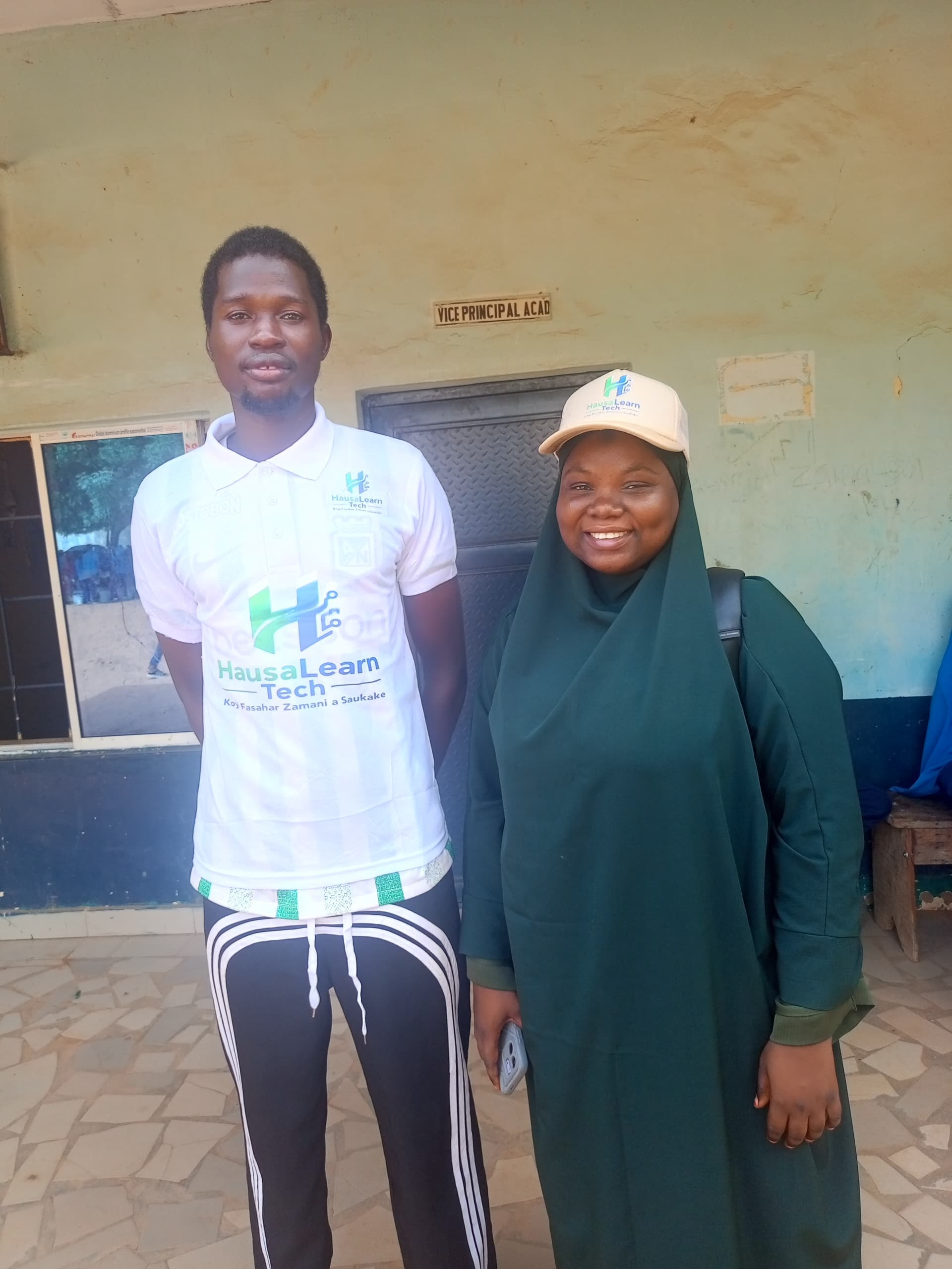 Two HausaLearn Tech team members in branded shirt and cap at a school